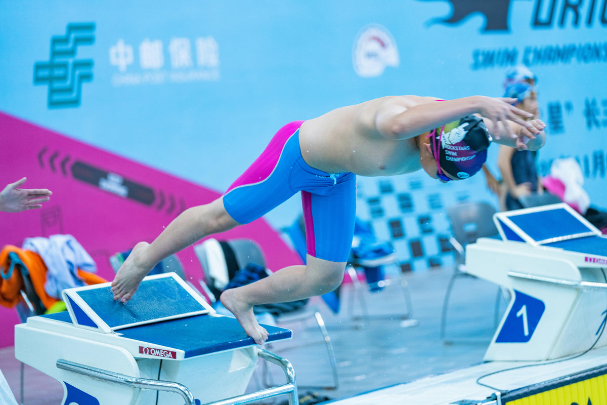 Competitive swimmers crouched on starting blocks before a race at an indoor swim meet